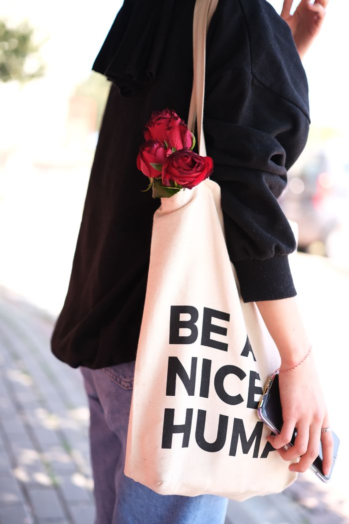 Stylish woman carrying a tote bag with red roses, promoting positivity with 'Be A Nice Human'.