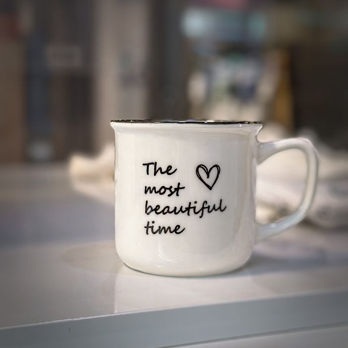 White ceramic mug with 'The most beautiful time' printed, featuring a heart design.